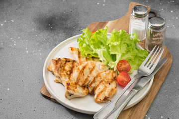 Grilled chicken fillet with greens on a white plate. Gray background