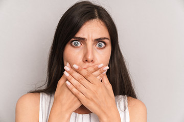 Image closeup of scared woman with long dark hair covering her mouth with fear