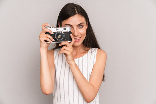 Image of young brunette woman wearing dress smiling and taking photo on retro camera
