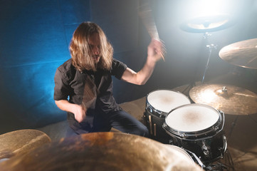 Portrait of a long-haired drummer with chopsticks in his hands sitting behind a drum set. Low key....
