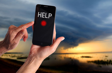 Smartphone in a female hand with a signal for help on a background of dramatic stormy sky