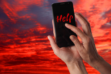 Smartphone in a female hand with a signal for help on a background of dramatic stormy sky