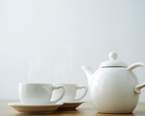 cup and saucer with teapot on wooden table.