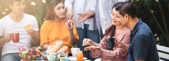 Family lunch outdoor. Married mix race couple with grand parents. White man, Asian pregnant woman with senior asian, white couple in tropical garden.Talking and laughing. Banner frame. Light leaks.