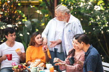 Family lunch outdoor. Married mix race couple with grand parents. White man, Asian pregnant woman with senior asian, white couple in tropical garden. Eating bread.