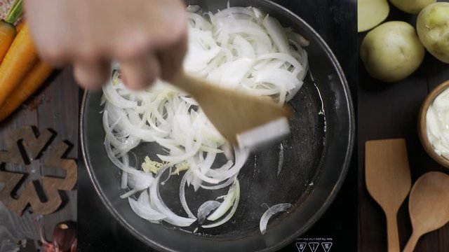 Flat lay video: chef stirs chopped onion by wooden kitchen spatula on the hot pan, tabletop of cooking vegetarian food, fried onions, blanch vegetables, Full HD Prore 422 HQ