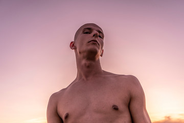 Fototapeta premium Portrait of a young beautiful male model outdoors by the sea at sunset