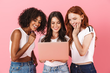 Cute smiling young three multiethnic girls friends posing isolated over pink wall background using...