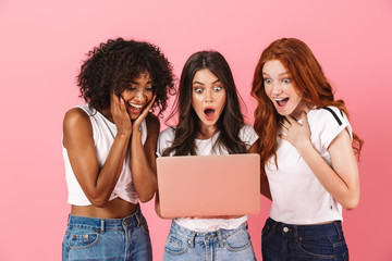 Shocked surprised emotional young three multiethnic girls friends posing isolated over pink wall...