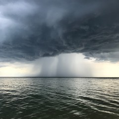 Storm on the sea. Calm before the storm. Dark, thunderstorm clouds, rain in the distance.