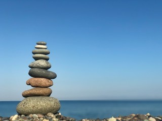 Fototapeta na wymiar Marine theme: stones on the shore. The stones are stacked in a pyramid against the background of the sea. Pyramid of small stones on the beach. The concept of harmony of balance and meditation. 