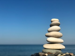 Marine theme: stones on the shore. The stones are stacked in a pyramid against the background of the sea. Pyramid of small stones on the beach. The concept of harmony of balance and meditation. 