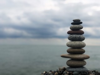 Marine theme: stones on the shore. The stones are stacked in a pyramid against the background of the sea. Pyramid of small stones on the beach. The concept of harmony of balance and meditation. 