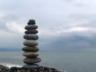 Marine theme: stones on the shore. The stones are stacked in a pyramid against the background of the sea. Pyramid of small stones on the beach. The concept of harmony of balance and meditation. 