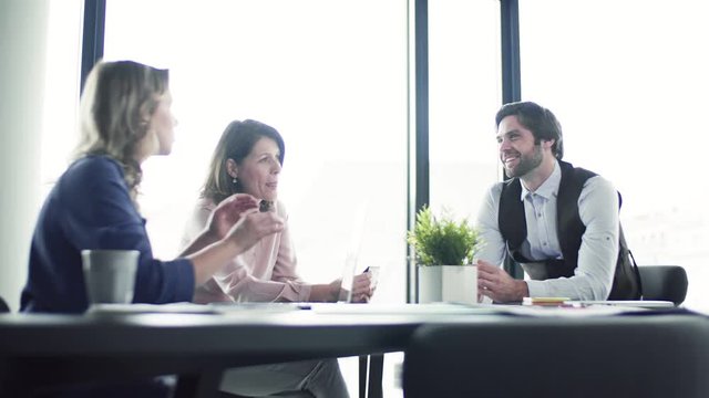 A group of business people with laptop sitting in an office, talking.