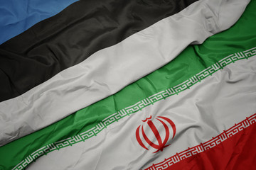 waving colorful flag of iran and national flag of estonia.