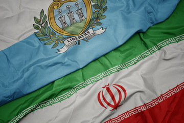 waving colorful flag of iran and national flag of san marino.