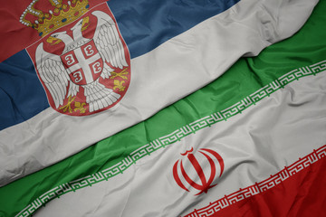 waving colorful flag of iran and national flag of serbia.