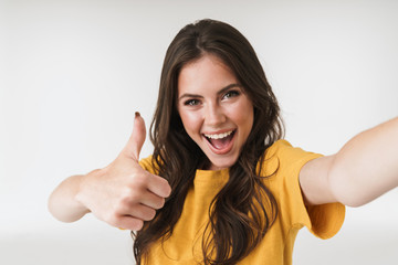 Image of excited brunette woman smiling and showing thumb up while taking selfie photo