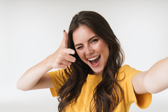 Image of beautiful brunette woman smiling and pointing finger at camera while taking selfie photo