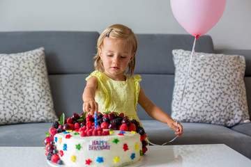 Sweet baby girl in cute yellow dress, celebrating her second birthday with homemade cake