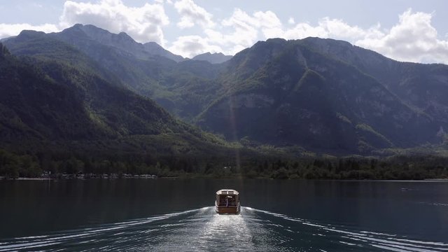 Aerial follow footage of a small tourist Boat cruising slowly at Lake Bohinj, Slovenia.