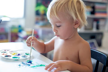 Little toddler boy, painting at home, learning coordination of moves