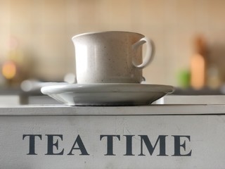 Time to drink tea. Teacup, with the bottom of the inscription "Tea time", on a blurred background.