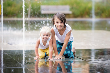 Cute toddler boy and older brothers, playing on a jet fountains with water splashing around