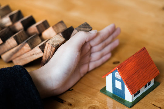 Close-up Of Business Woman Hand Stopping and Covering The Wooden Blocks From Falling On House Model, insurance concept.