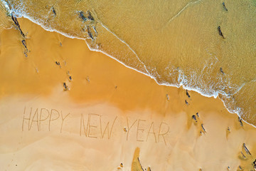 Aerial top shot from ocean waves and handwritten Happy New Year at the beach