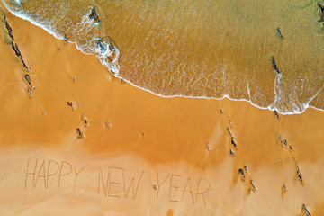 Aerial top shot from ocean waves and handwritten Happy New Year at the beach