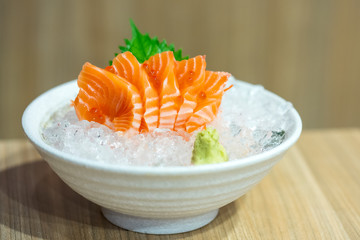 A delicious famous traditional Japanese food name Salmon sashimi sliced and served with wasabi paste on crushed ice in white bowl in Japan restaurant. Closed up with show texture. Front view.