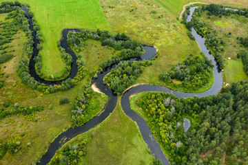 Top view drone shot of a green field, forest and river