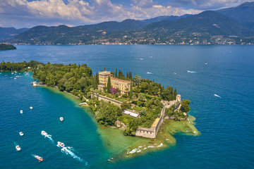 Unique view of the island of Garda. In the background is the Alps. Resort place on Lake Garda north of Italy. Aerial photography. - obrazy, fototapety, plakaty