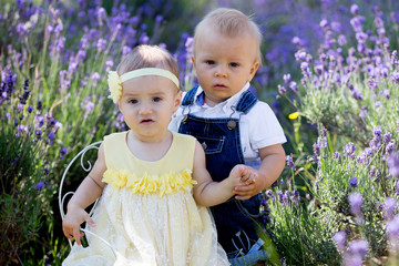 Happy smiling baby twins, boy and girl, sitting on vintage chair in lavender field
