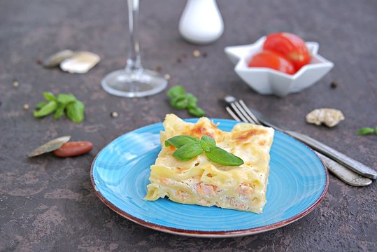 Fish lasagna with salmon and cheese on a blue plate on a dark brown concrete background. Fish and seafood recipes. Italian food