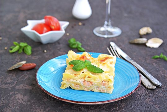 Fish lasagna with salmon and cheese on a blue plate on a dark brown concrete background. Fish and seafood recipes. Italian food