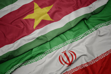 waving colorful flag of iran and national flag of suriname.