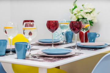 Close-up of served table. Lemon water in wine glasses. Plates and cups. Flowers in vaze.