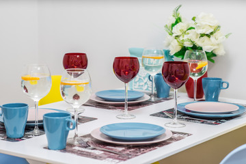 Close-up of served table. Lemon water in wine glasses. Plates and cups. Flowers in vaze.