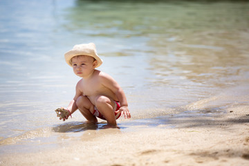 Sweet toddler boy, playing in shallow water on a tropical beach