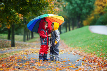 Two adorable children, boy brothers, playing in park with umbrella