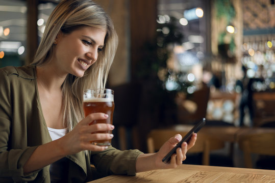Happy woman reading text message on mobile phone while sitting in a bar