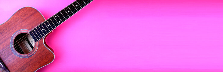 Fototapeta premium Acoustic guitar resting against a blank pink background with copy space.