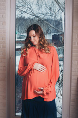 Fototapeta premium a pregnant woman stands thoughtfully at the window, playing with curtains. The concept of a healthy lifestyle, IVF