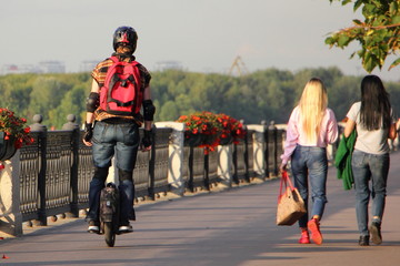 A young man with helmet and protective equipment rides on electric mono wheel on an asphalt road in Park near two girls pedestrian on a summer day - safety on personal urban transport © Ilya