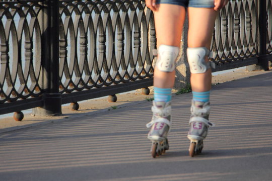 Young girl rollerblading, woman legs in protective kneepads closeup on an asphalt road in Park on a summer day - sporty lifestile