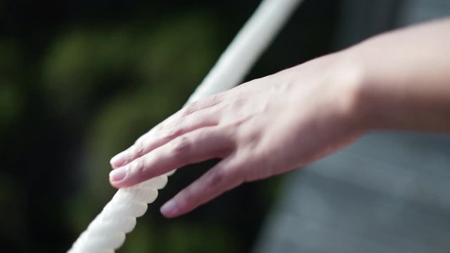 Acompanhamento de mão de mulher a andar e a tocar numa corda branca de um passadiço de madeira com uma lente de grande desfoco. Em Portugal.