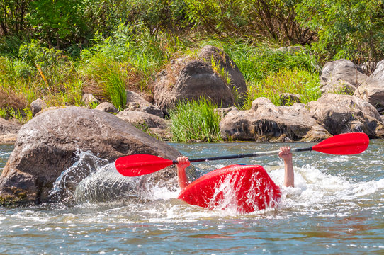 Playboating. A man sitting in a kayak with oars in his hands performs exercises on the water. Kayaking freestyle on whitewater. Eskimo roll.
